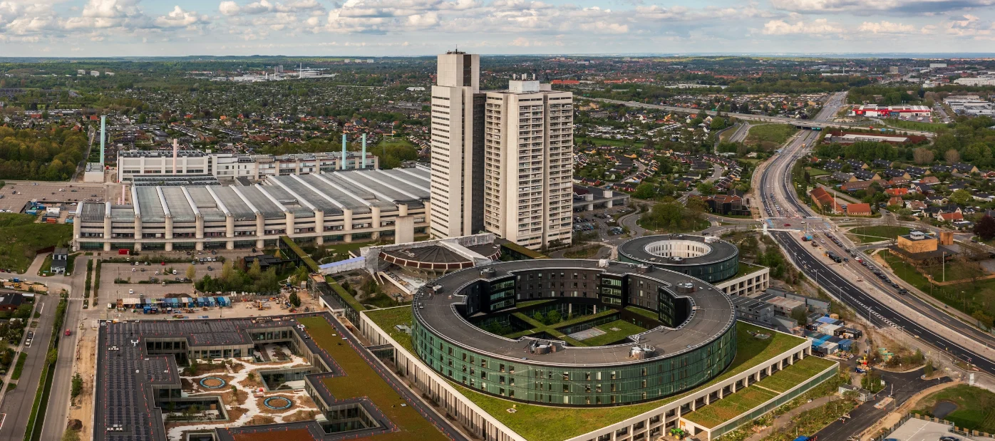 Herlev Hospital set fra luften, med det ikoniske højhus og den cirkulære hospitalsbygning i forgrunden.